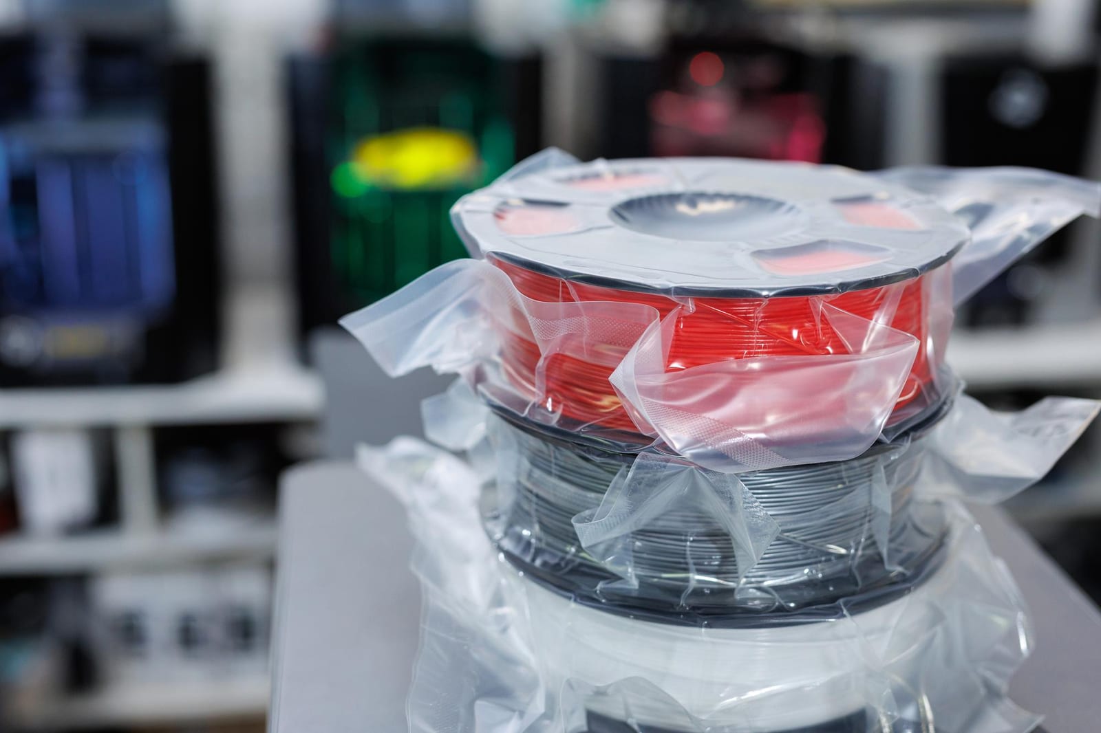 Bobinas de filamento 3D lacradas a vácuo em tons de vermelho, cinza e branco empilhadas